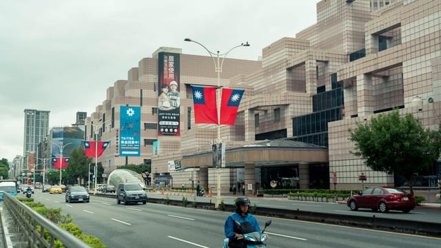 Taipei street scene featuring busy traffic, prominent mall, and national flags.