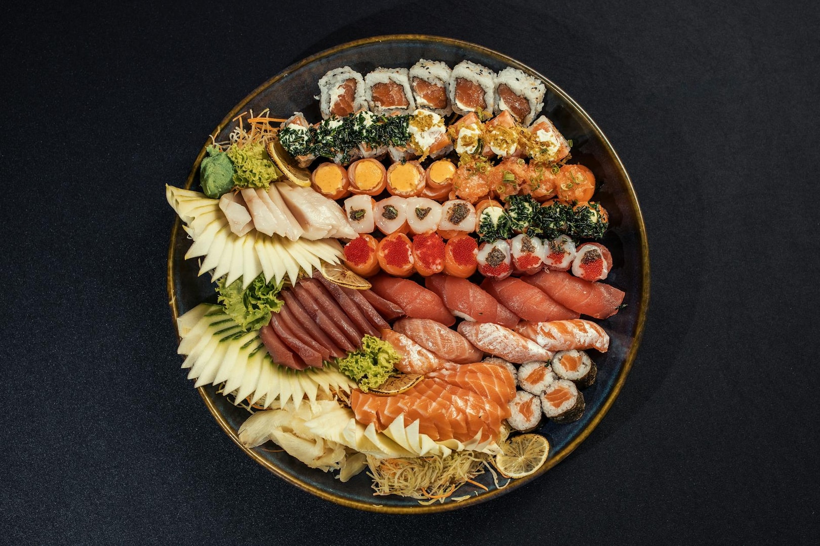 Colorful sushi platter featuring various rolls and sashimi, beautifully arranged on a dark surface.