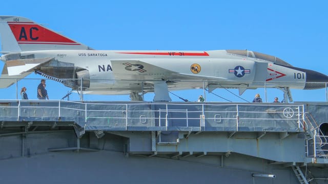 Fighter jet displayed on the USS Saratoga aircraft carrier deck with visitors exploring the site.