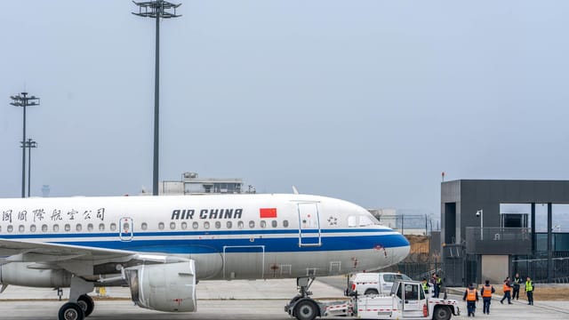 Air China airplane being maneuvered on the runway by ground staff at an airport.