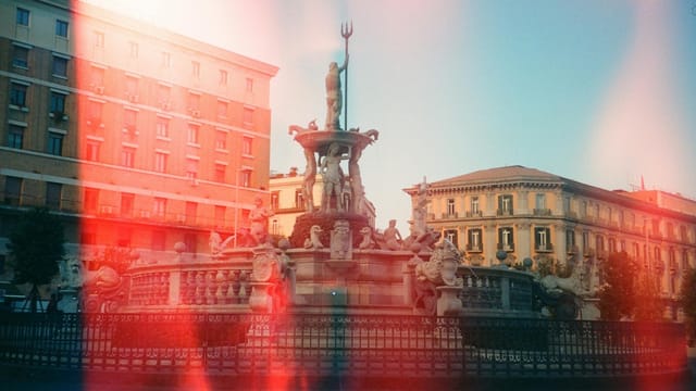 Artistic film photo of a Neptune fountain with classic architecture under a clear sky.