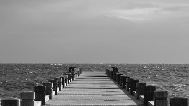 Monochromatic view of a peaceful pier extending into the ocean under a cloudy sky.