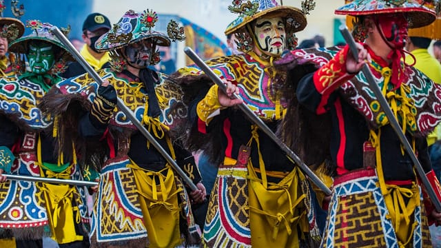 Masked performers in colorful traditional costumes parade during a vibrant cultural festival in Taiwan.