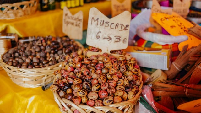 Close-up of colorful nutmeg in baskets at a lively marketplace with handwritten signs.