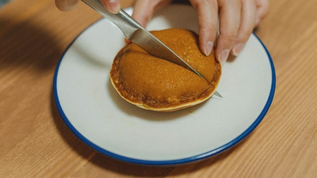 Close-up of hands cutting a dorayaki pancake revealing sweet filling, on a white plate. Authentic Japanese dessert.