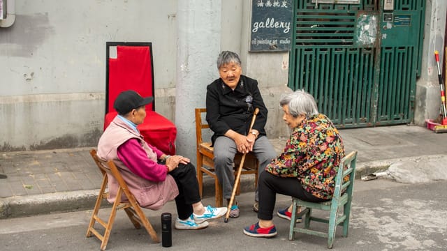 Three senior women engaged in conversation on a street in Shanghai, China.