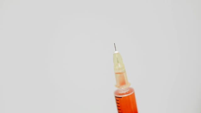 Detailed image of a syringe needle with red liquid against a soft background.