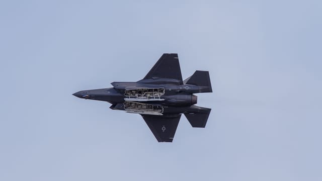 An F-35 fighter jet mid-flight showcasing its aerodynamic design against a clear sky.