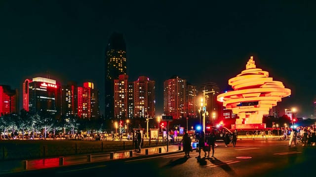 Vibrant cityscape image of May Fourth Square in Qingdao illuminated at night.