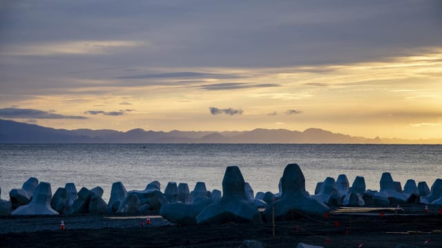 Scenic sunrise with coastal breakwaters against a tranquil sea and distant mountains.