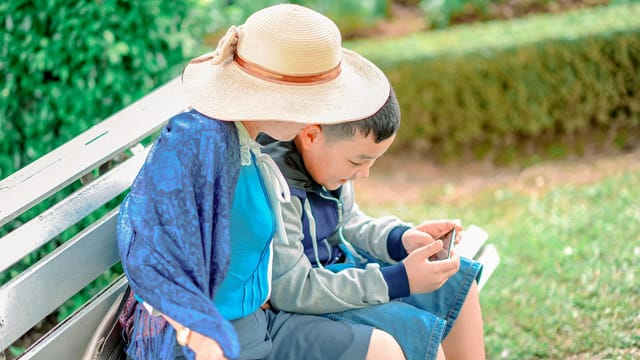A mother and son bond while enjoying a sunny day at the park, sitting on a bench.