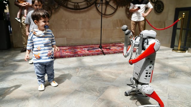 A young boy engages with a humanoid robot during an indoor tech exhibition, symbolizing future innovation.