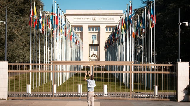 Man photographs the United Nations Office with international flags in Geneva, Switzerland.