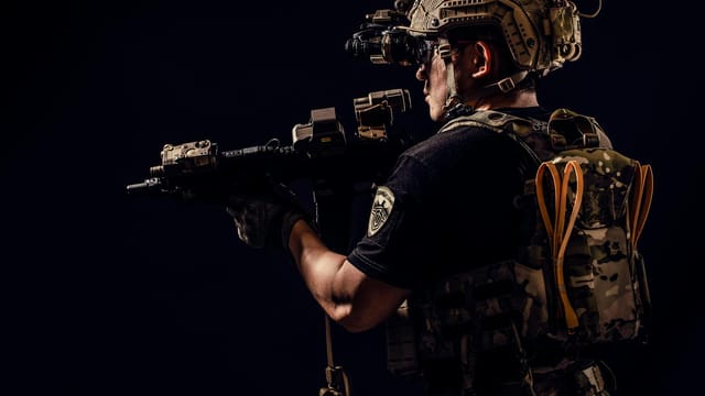 Portrait of a soldier in tactical gear holding a rifle in a studio setting.