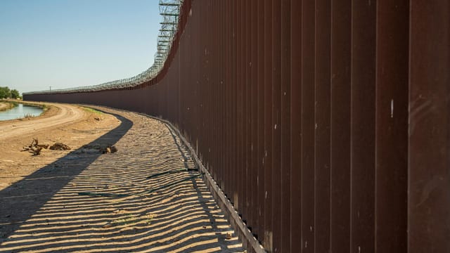 Long view of a steel border wall under clear skies, emphasizing solitude and division.