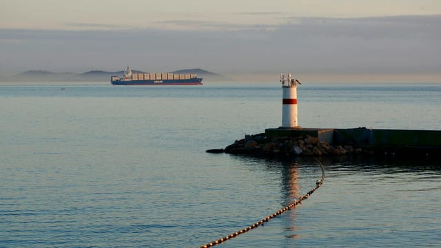 Container ship passing by a lighthouse in İstanbul, Türkiye, at dawn.