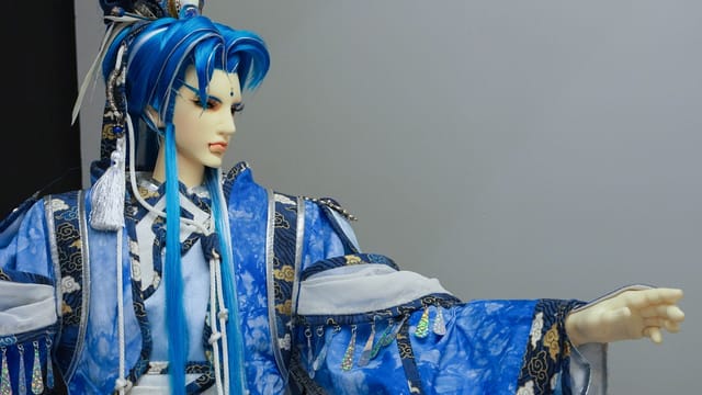 Intricately designed Asian doll in blue traditional clothing against a gray background.