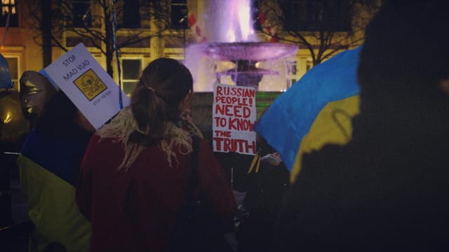 Protesters in London rally against war, holding placards under city lights, expressing solidarity with Ukraine.