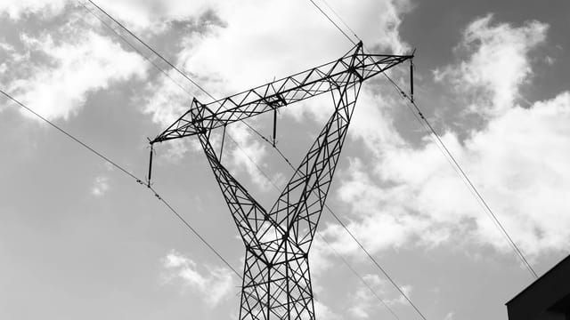 A high voltage power line towering against a dramatic cloudy sky in a black and white composition.