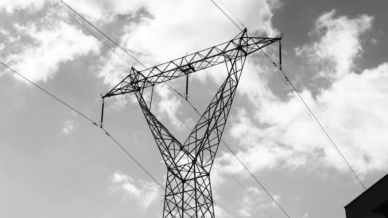 A high voltage power line towering against a dramatic cloudy sky in a black and white composition.