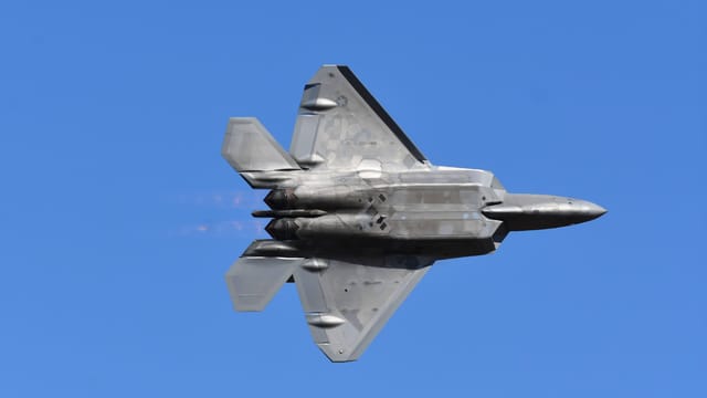 A dynamic capture of an F-22 Raptor soaring through a clear blue sky, showcasing its advanced design.