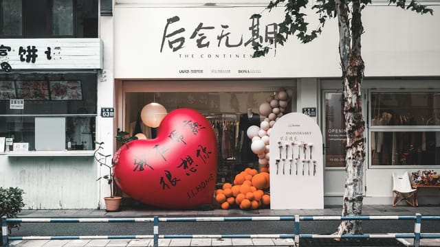 Street view of a modern clothing store with a large heart decoration and balloons outside.