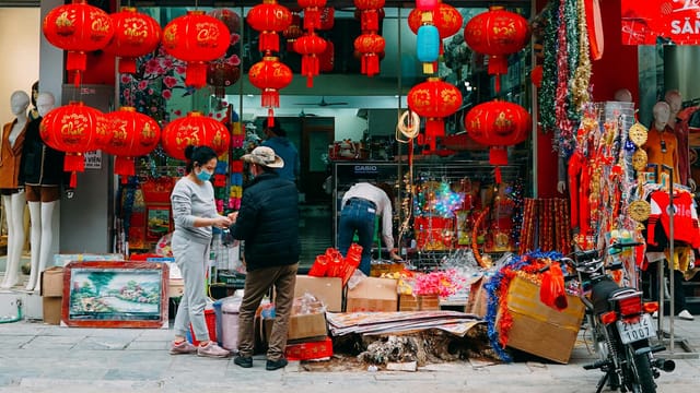 Colorful Chinese lanterns at an outdoor market with people shopping festive decorations.