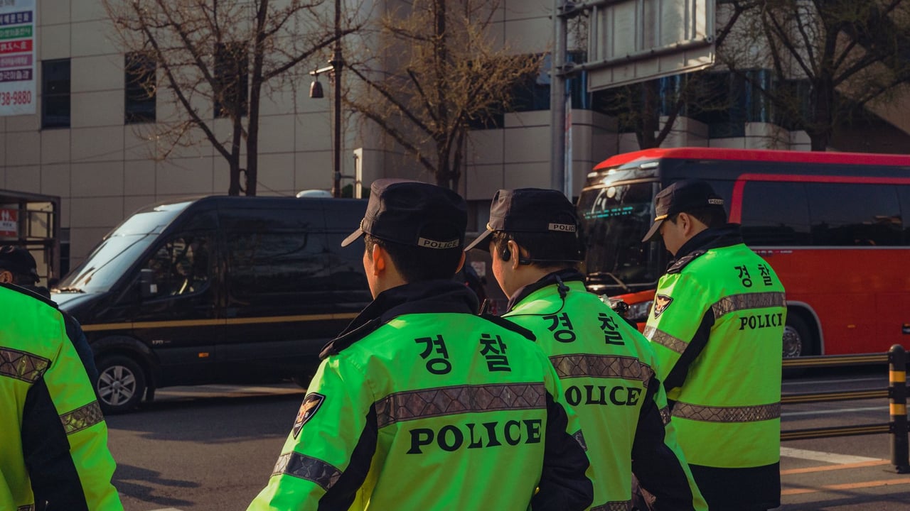 Uniformed police officers in vibrant gear monitor a busy Seoul street during the day.