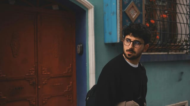 A trendy man in eyewear walking by colorful doorways in Istanbul's vibrant streets.