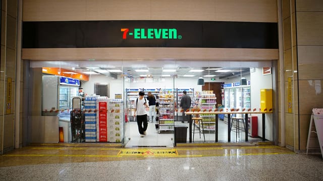 Indoor view of a 7-Eleven store entrance with people shopping and products displayed.