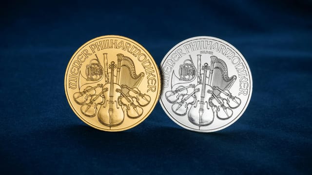 Close-up of gold and silver Wiener Philharmoniker coins displayed on blue velvet cloth.