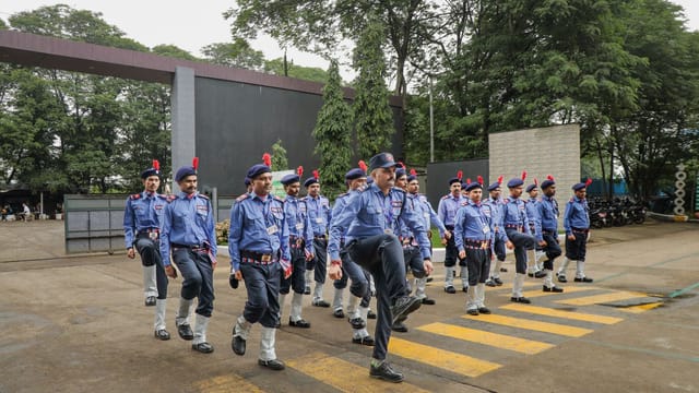 A group of Indian police cadets perform a synchronized march outdoors under cloudy skies.