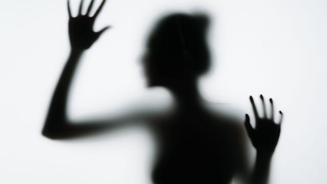 A conceptual silhouette of a woman pressing her hands against a smoky glass panel, evoking mystery.