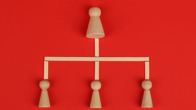 Conceptual depiction of hierarchy using wooden pieces on a vibrant red background.