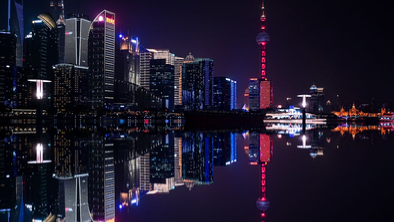 Dazzling night view of Shanghai's Pudong skyline with the iconic Oriental Pearl Tower reflecting on the water.