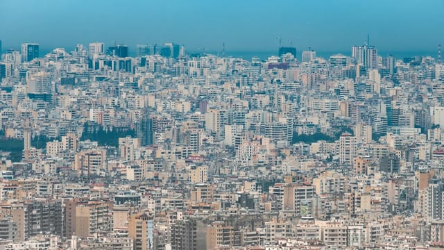 A sprawling aerial view of Beirut's dense urban skyline under a clear blue sky.