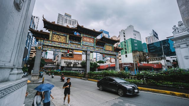 A bustling street scene with Chinatown gate, people, cars, and high-rise buildings under a cloudy sky.