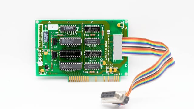 Close-up of a vintage Apple circuit board with a multicolored ribbon cable on a white background.