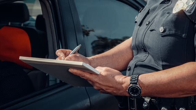 Close-up of a police officer writing a ticket by a car window. Law enforcement scene.