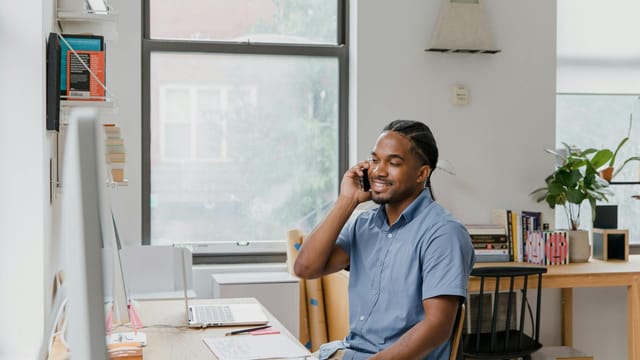 Adult man engaged in office work, speaking on phone, showcasing a professional environment.