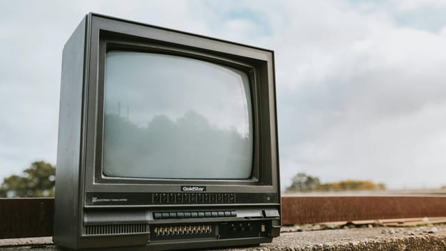 Old CRT television set placed outdoors with a cloudy sky backdrop, evoking nostalgia.