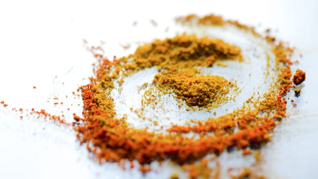 A vibrant array of colorful spices including turmeric and curry powder on a white background.