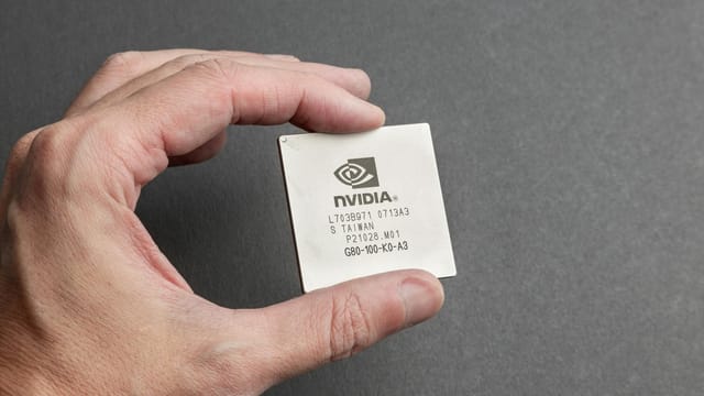 A close-up view of a person holding an Nvidia chip with a gray background.
