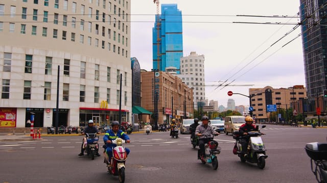 Motorcyclists navigating a bustling intersection in Shanghai, China, surrounded by modern skyscrapers.