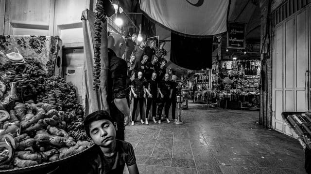A serene black and white portrayal of a boy in the bustling İsfahan bazaar at night.