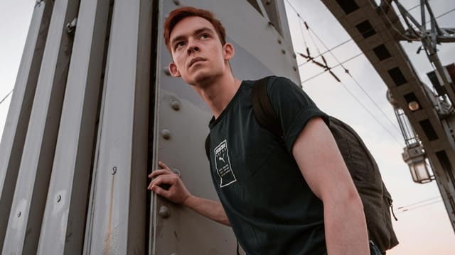 Young backpacker in casual wear standing on a bridge in Saint Petersburg, Russia, with a determined look.