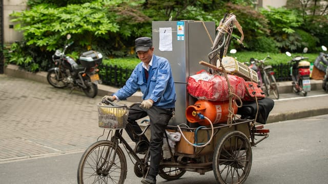 Man transporting goods on a tricycle in Shanghai, showcasing urban life and commerce.