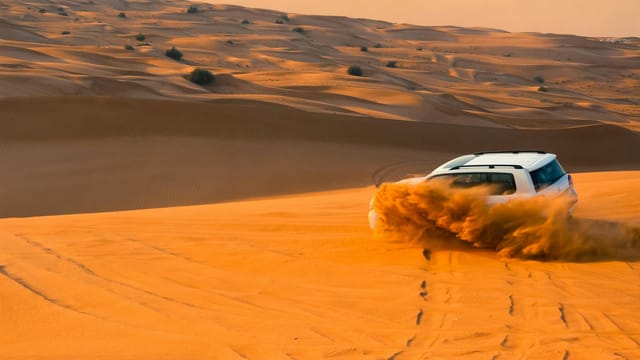 A thrilling SUV driving through the sand dunes of Dubai's desert landscape at sunset.