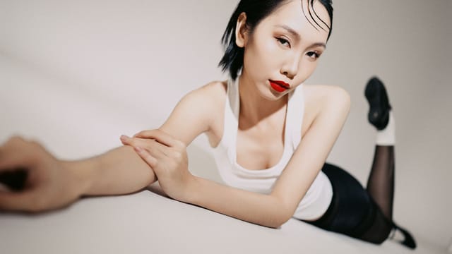 Portrait of a fashionable woman in a white tank top and red lipstick, stretching elegantly.