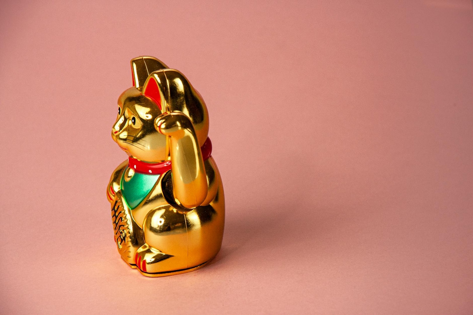 Gold Maneki Neko figurine, a Japanese lucky cat, displayed on a pastel pink background.